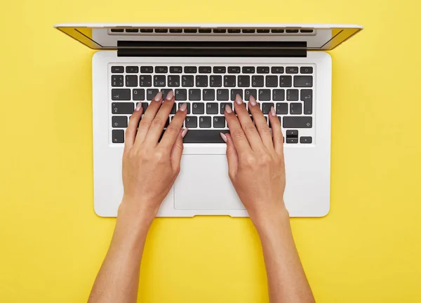 Mulher mãos impressão em laptop de pé no fundo amarelo — Fotografia de Stock