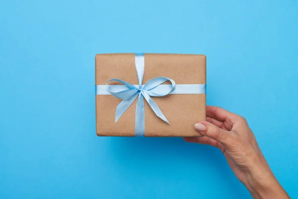 Hands of female holding a gift box over blue background — Stock Photo, Image