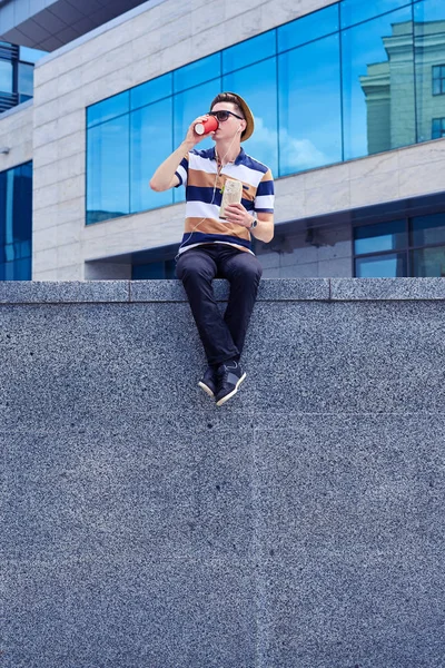 Joven sosteniendo bocadillo con café, sentado al aire libre —  Fotos de Stock