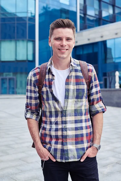 Ragazzo sorridente in camicia a quadri con zaino in piedi vicino ai cespugli — Foto Stock