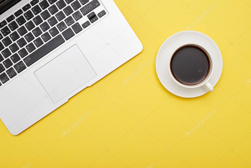 Laptop and cup of coffee on yellow background