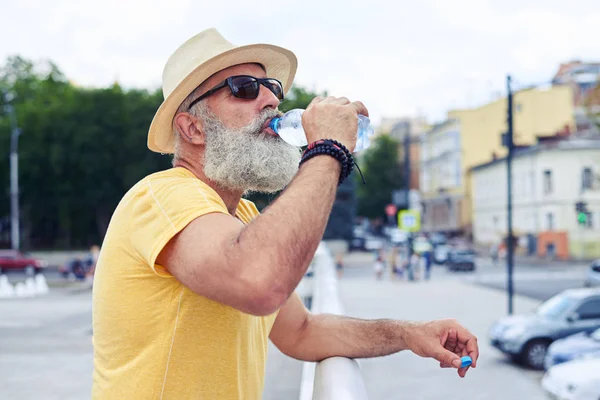 Hombre mayor bebiendo agua de una botella de plástico con un ci urbano —  Fotos de Stock