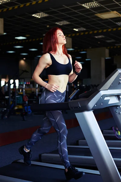 Ganska smal tjej tränar på löpband på gymmet och smili — Stockfoto
