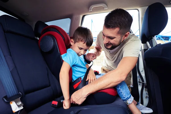 Concentrated father helps his son to fasten belt on car seat — Stock Photo, Image