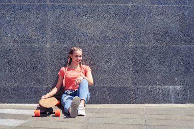 Kaykay ile duvar altında otururken çok güzel kadın