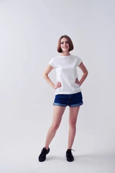 Docela kaštanové mladá žena pózuje v džínách šortky a bílé T-s — Stock fotografie