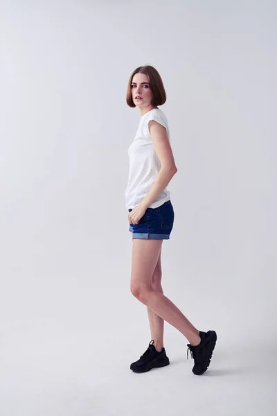 Гарна молода жінка позує в джинсових шортах і білій футболці — стокове фото