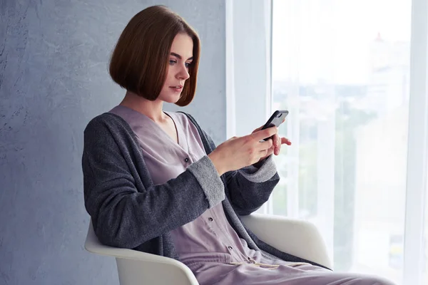 Vacker ung kvinna med telefon och sitter på fåtölj — Stockfoto