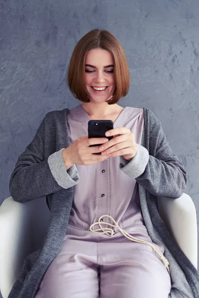 Lachende dame met behulp van smartphone en zittend op fauteuil — Stockfoto