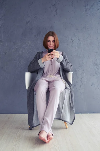 Relaxed woman using smartphone and sitting on armchair — Stock Photo, Image