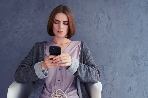 Koncentrerad kvinna med smartphone och sitter på fåtölj — Stockfoto