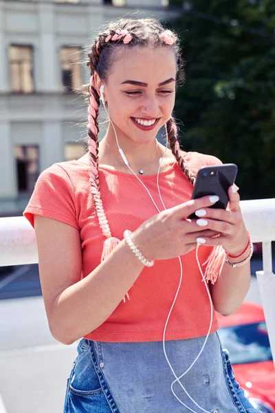 Modieuze meisje in hoofdtelefoon surfen in smartphone — Stockfoto