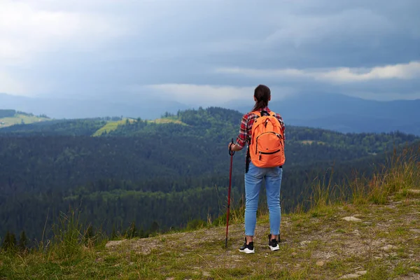 Woman with hiking poles standing on edge of mountain