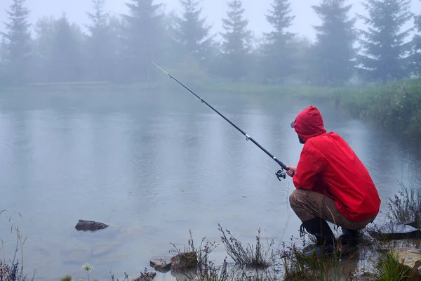 Сконцентрированный человек сидит и ловит рыбу на озере — стоковое фото