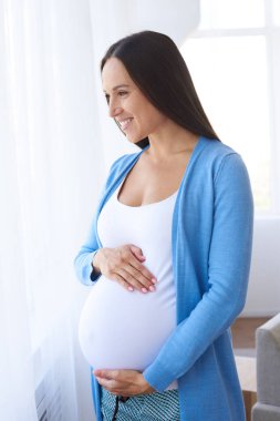 Pencere yanında duran gülümseyen hamile kadın