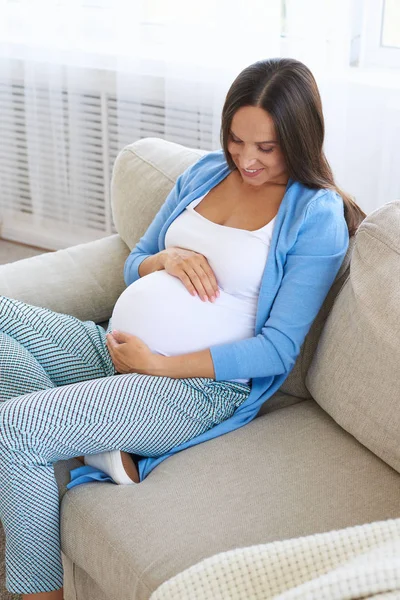 Femme enceinte touche le ventre avec amour sur le canapé — Photo