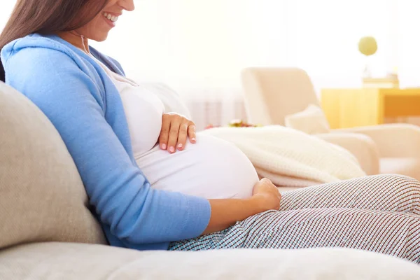 Schwangere hält Hände auf ihrem Bauch, während sie sich entspannt auf — Stockfoto