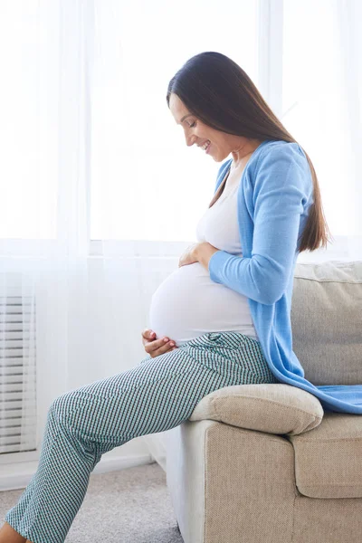 Mulher olhando para a barriga no sofá — Fotografia de Stock