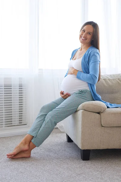 Widok z boku w ciąży kobieta siedzi na kanapie — Zdjęcie stockowe