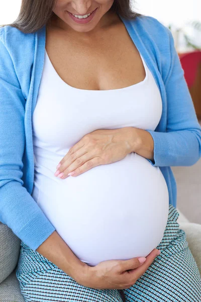 Karnına tutarak kanepede oturan kadın