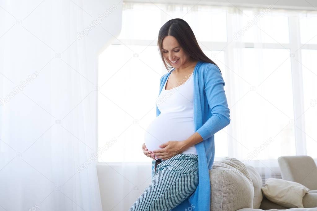 Pregnant woman watching her belly near a window