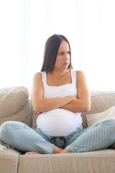 Upset pregnant woman sitting on sofa with hands crossed — Stock Photo, Image