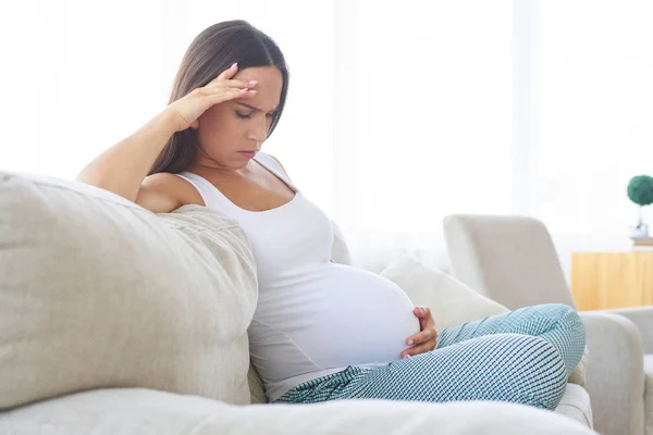 Femme enceinte inquiète assise sur le canapé — Photo