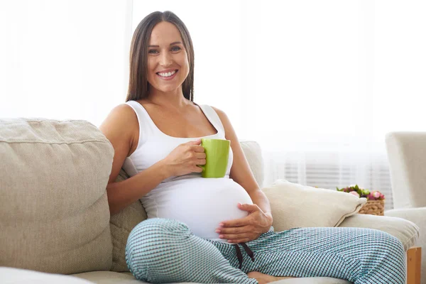 Mulher grávida sentada com caneca de chá colocada na barriga — Fotografia de Stock