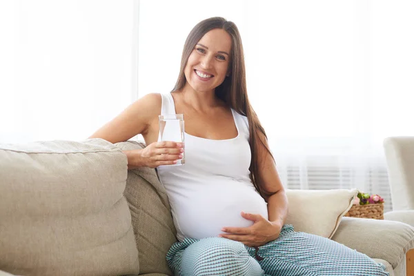 孕妇拿杯水在沙发上放松 — 图库照片