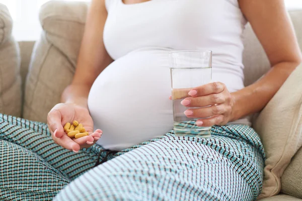 Schwangere Hand mit Glas Wasser und Tabletten — Stockfoto