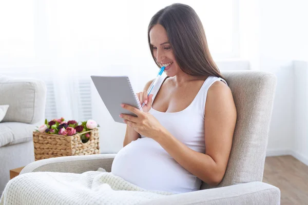 Heerlijke zwangere vrouw met pen holding notitieblokje — Stockfoto