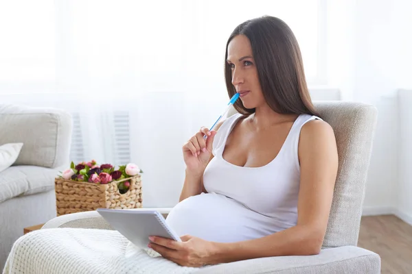 Soñando mujer embarazada escribiendo nombres de bebé en cuaderno — Foto de Stock