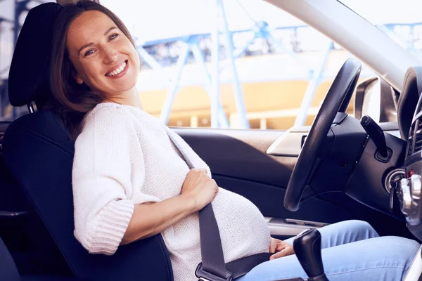 うれしそうな妊娠中の女性の車の運転席でポーズ — ストック写真