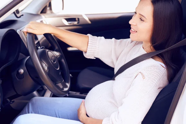 Happy pregnant woman with hand on belly driving car — Stock Photo, Image