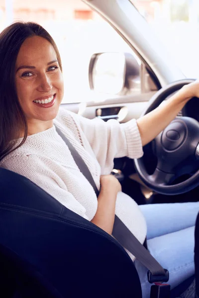 Zwangere vrouw in auto houdt wiel draaien rond het glimlachen op zoek — Stockfoto