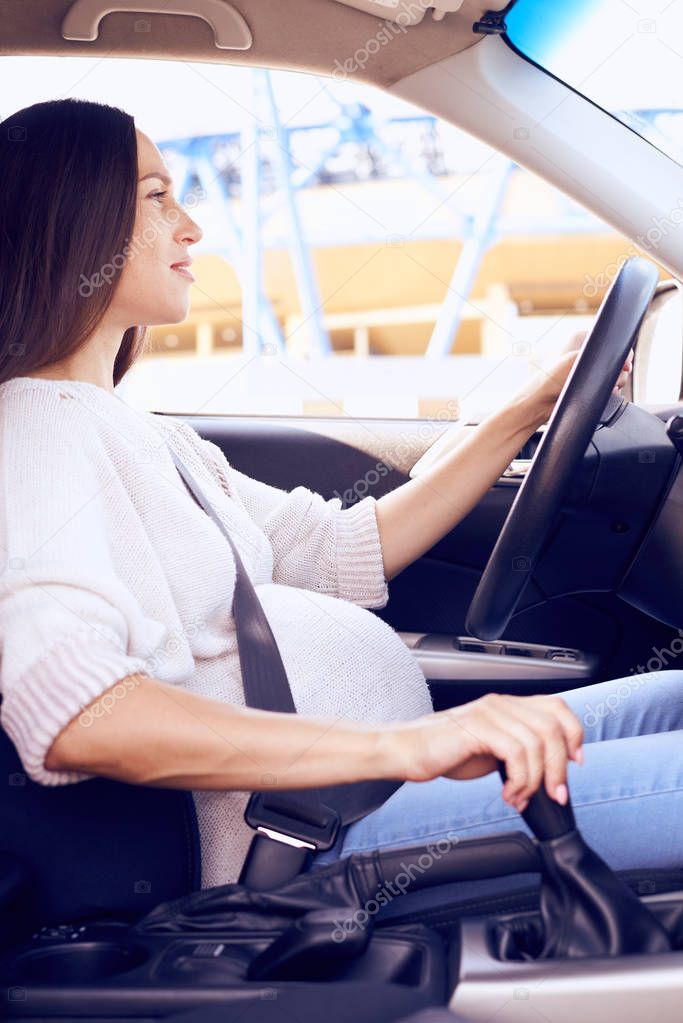 Attentive pregnant woman driving car in daytime 