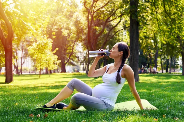 Sportive pregnant woman drinking water in park — Stock Photo, Image