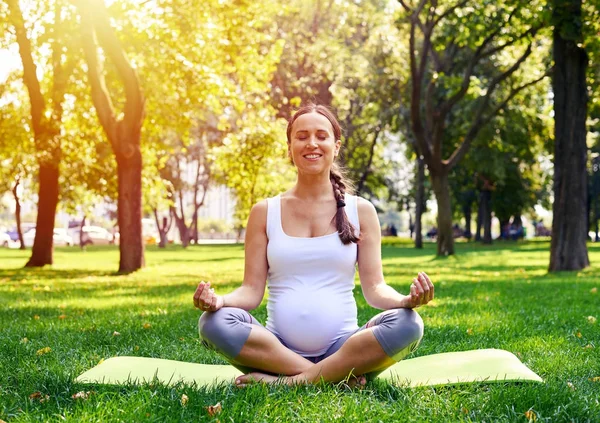 Mujer embarazada feliz sentada en pose de loto en el parque —  Fotos de Stock