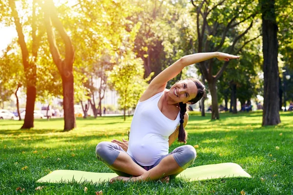 Femme enceinte en bonne forme s'étirant sur tapis de yoga à l'extérieur — Photo