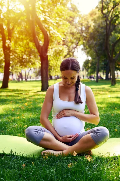 Charmante zwangere vrouw bedrijf buik zittend in yoga pose — Stockfoto
