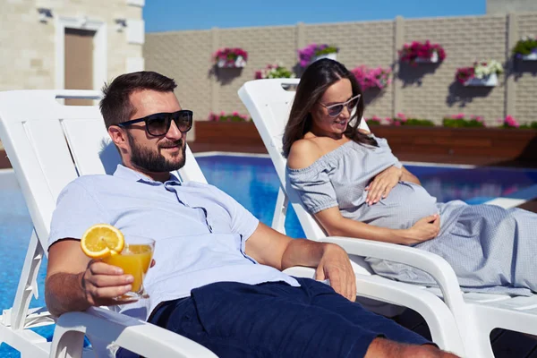 Mann und schwangere Frau entspannen sich auf Lounge am Pool — Stockfoto