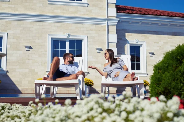 Happy couple talking while relaxing on lounge chairs in front of — Stock Photo, Image