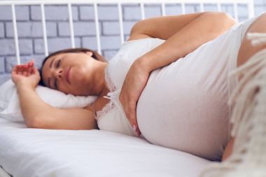 Genç hamile kadın yatakta uyuyor.