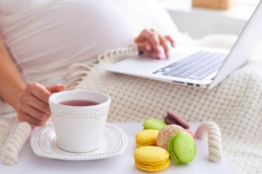 Pregnant woman using laptop with tray of colorful macaroons and  clipart