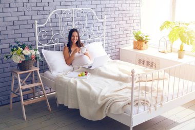 Dizüstü bilgisayar kullanarak ve yatak odasında kahvaltı hamile kadın