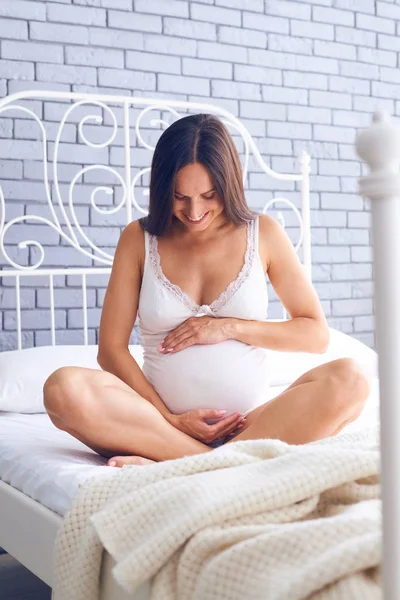 Happy těhotná žena hospodářství břicho na postel — Stock fotografie