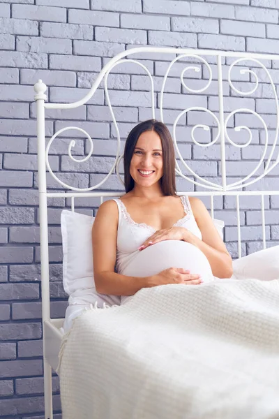 Mujer embarazada sonriente sentada en la cama en casa — Foto de Stock