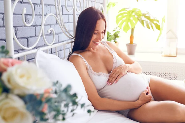 Feliz mujer embarazada está descansando en casa en la cama — Foto de Stock