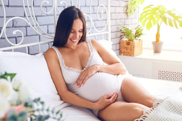 Schöne Frau, die ihren schwangeren Bauch zu Hause liebevoll betrachtet — Stockfoto