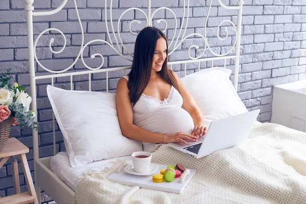 Femme enceinte utilisant un ordinateur portable et prenant le petit déjeuner au lit — Photo